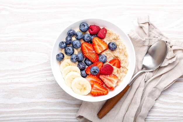 Oatmeal porridge with fruit and berries on white wooden table