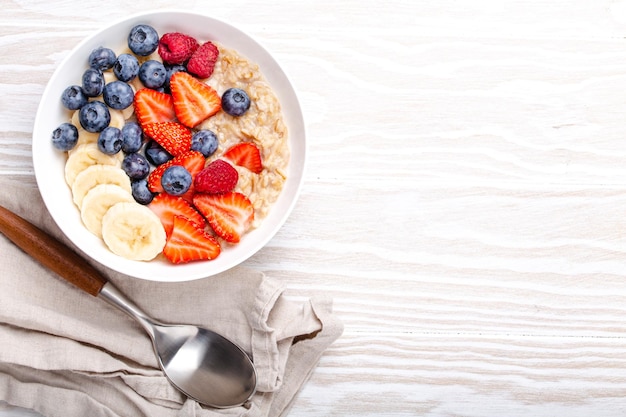 Oatmeal porridge with fruit and berries on white wooden table