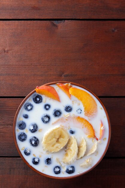 Oatmeal porridge with milk and fruit on wooden background Milk oatmeal with blueberries and fruits in clay bowl Copy space