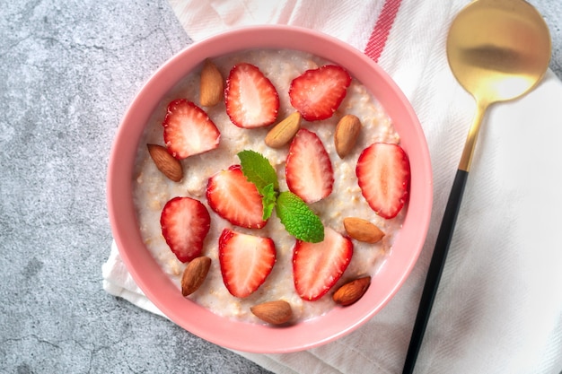 Oatmeal porridge with strawberries almonds mint leaf in pink bowl spoon and napkin with red stripes ...