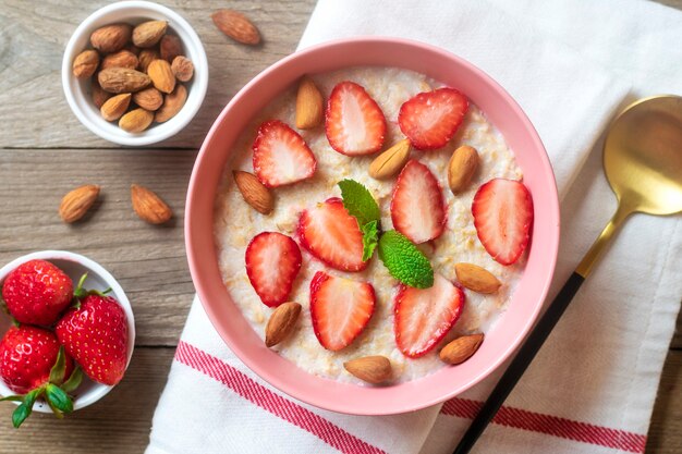 Oatmeal porridge with strawberries almonds mint leaf in pink bowl spoon and napkin with red stripes ...