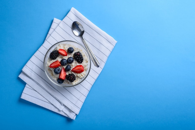 Oatmeal in transparent bowl with berries on white towel 