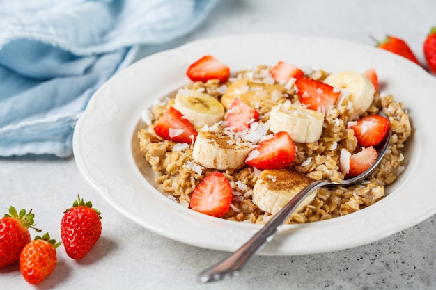 Oatmeal with banana, strawberries and peanut butter in white plate.