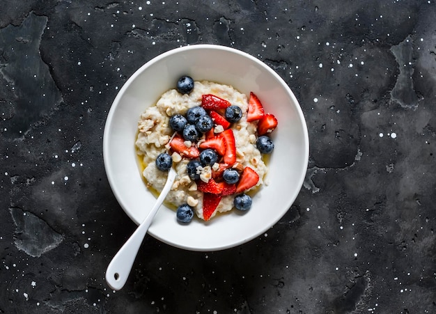 Oatmeal with berries nuts and honey on a dark background top view