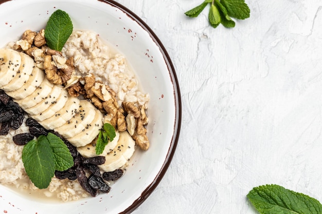 Oatmeal with dried raisins banana and walnuts decorated with mint Healthy diet vegetarian breakfast or snack Clean eating dieting vegan food concept top view