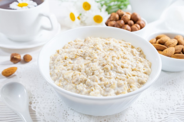 Oatmeal with nuts in bowl on white wooden table.