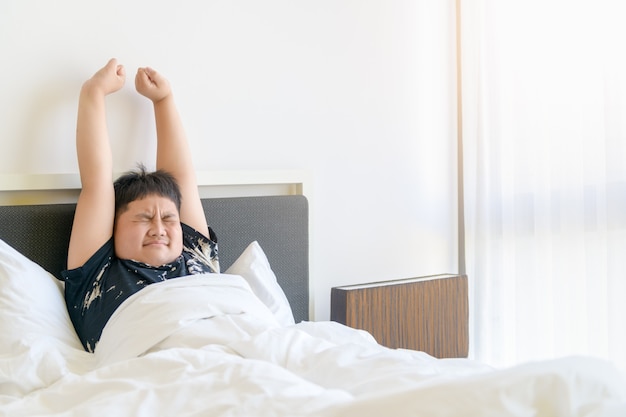 Obese boy wake up and stretch arm on bed in morning. lazy and rest