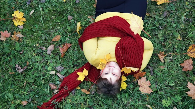 Obese girl with red scarf smiling lying on grass with maple leaves