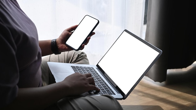 Obese woman working with laptop computer and using smart phone while sitting on wooden floor at home.