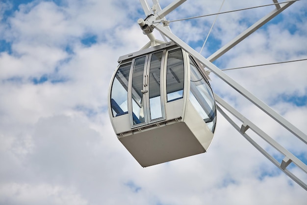 Observation wheel cabin close up, blue sky background. White passenger car of big Ferris wheel in amusement park, view from ground. Bird's Eye view attraction with panoramic observation