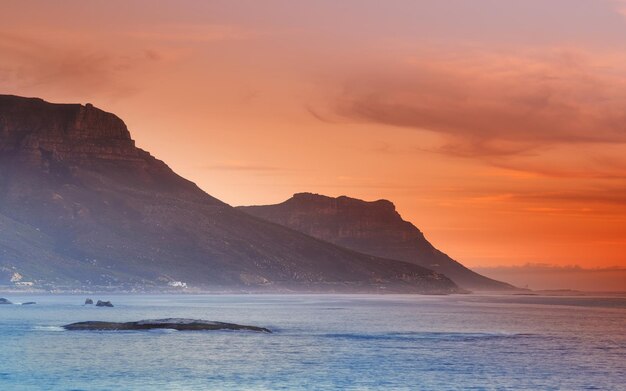 Photo ocean sunset and mountains in nature or sustainable environment and travel destination for vacation landscape sea or sunlight on water on beach calm or seascape of camps bay for tourist adventure