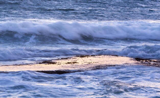 Ocean waves splash over calm rock shelf at dawn