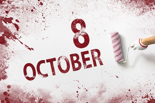 October 8th. Day 8 of month, Calendar date. The hand holds a roller with red paint and writes a calendar date on a white background. Autumn month, day of the year concept.