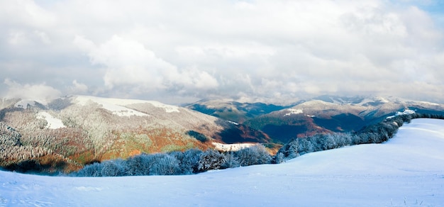 October mountain beech forest edge with first winter snow and last autumn colourful foliage on far mountainside