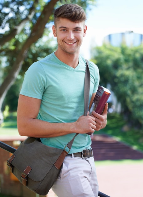 Off to class A handsome student standing outside on campus with a satchel and a textbook