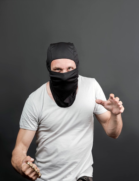 An offender attack with Brass knuckles. Metal brass knuckles in the hand of caucasian man in black mask. forbidden weapons in a fight, criminal. american man showing fist with brass knuckles. close up