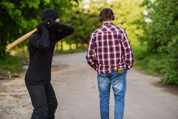 An offender in black clothes with a baseball bat in his hands attacks a man. Pickpocketing on the street during daytime.