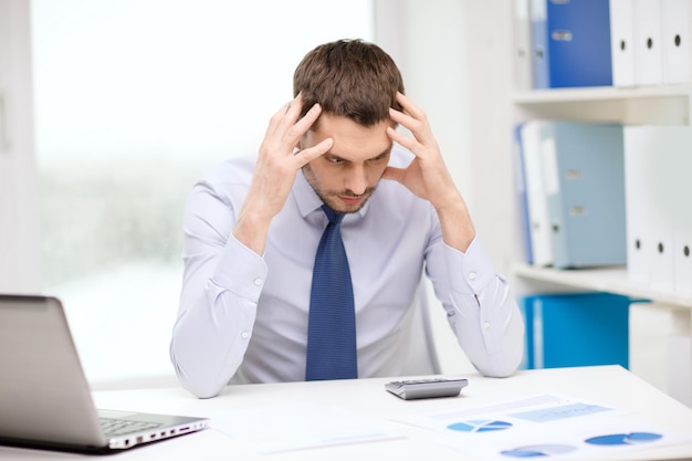 office, business, technology, finances and internet concept - stressed businessman with laptop computer and documents at office