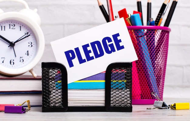 The office desk has diaries an alarm clock stationery and a white card with the text PLEDGE Business concept