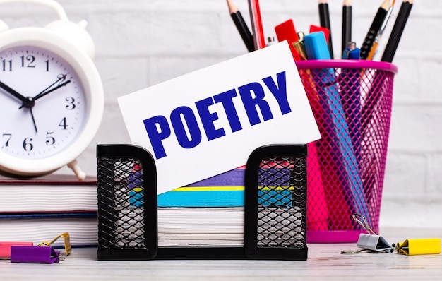 The office desk has diaries an alarm clock stationery and a white card with the text POETRY Business concept