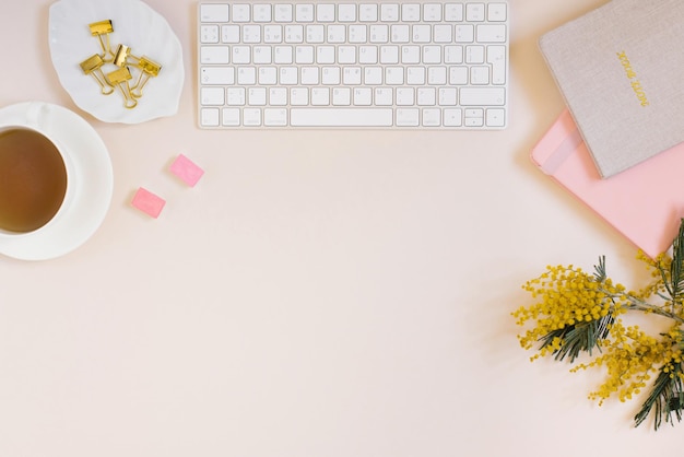 Office desk notebooks keyboard and colored pencils a cup of tea mimosa flowers on a beige background Minimal business concept for women Flat lay top view copy space