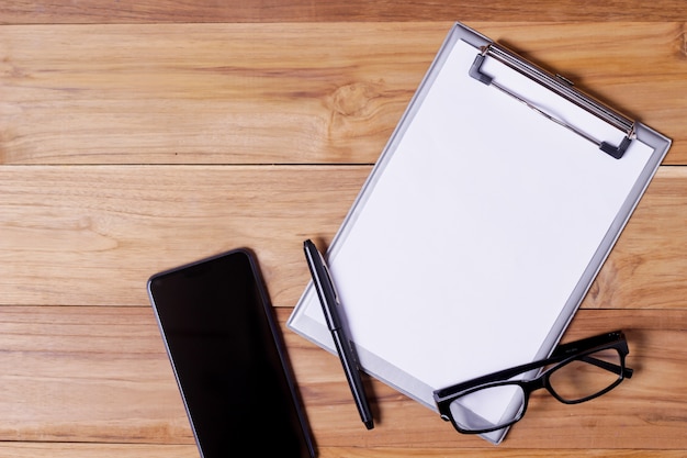 Office desk table with eye glasses short notepaper, pen and smartphone.