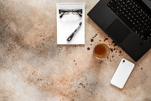 Office desk table with laptop notepad pen smartphone eyeglasses and glass of coffee top view mockup copy space