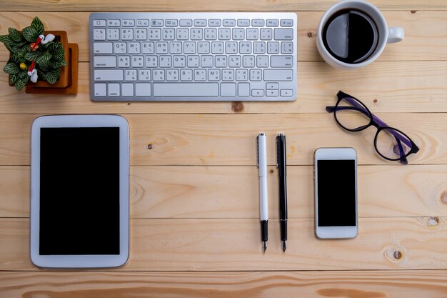 Office desk table with pen, keyboard on notebook, cup of coffee and flower. Top view with copy space (selective focus).