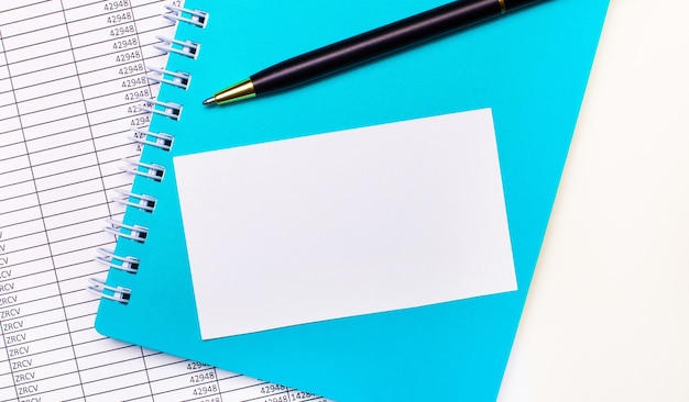 On the office desk there are reports, a light blue notepad, a black pen, and a white blank card with space to insert text. Stylish workplace. Business concept