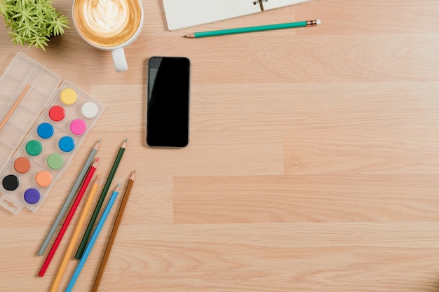 Office desk with smart phone, keyboard, notebook, water colour and cup of coffee.