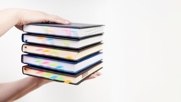 An office employee holds a stack of notebooks with colorful bookmarks on a light background