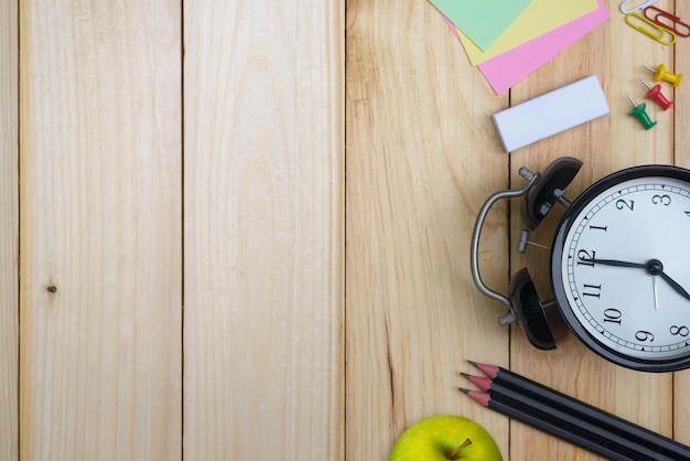 Office equipment and school supplies with clip board pencil pen rubber clock paper note and green apple on wood table background flat lay with space for text and banner design