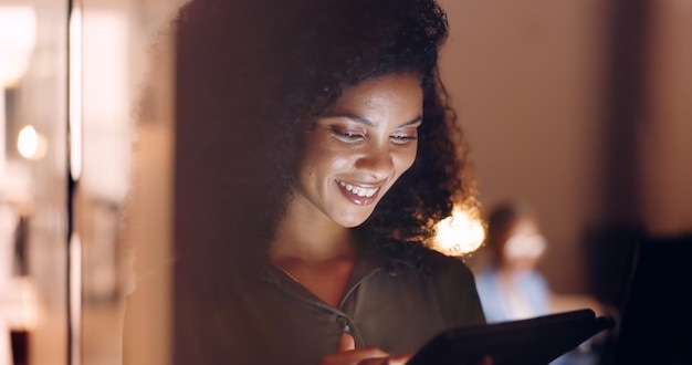 Office night and happy black woman on a phone at her job in the dark smiling about funny text Business technology and social media mobile app scroll of a person working late on a work break