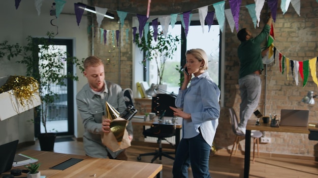 Office people preparing birthday party in coworking room couple unpacking boxes