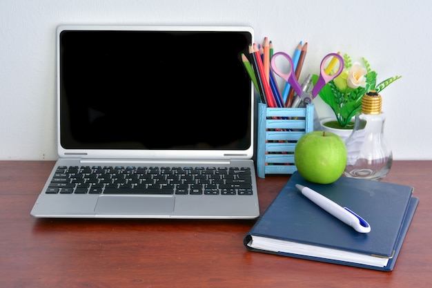 Office supplies, laptop with notebook and apple on wooden table