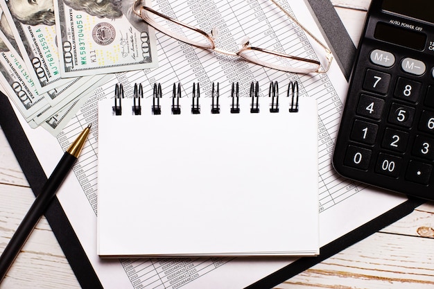 On the office table there is a calculator, a notebook with a place to insert text, a pen, glasses and dollars. Stylish workplace. Business concept