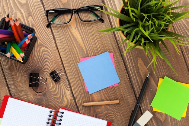 Office table with flower, blank notepad and supplies. View from above with copy space