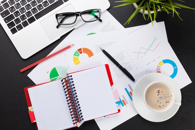 Office table with laptop coffee notepad and reports