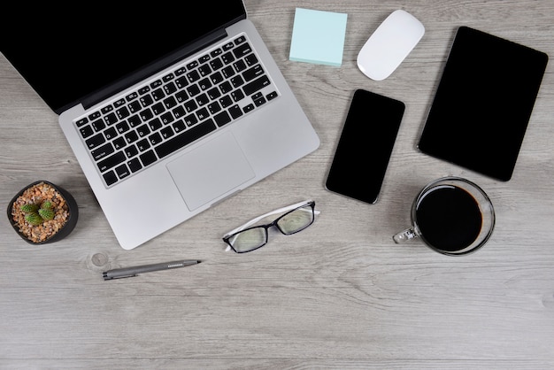 Office table with laptop computer, notebook, digital tablet, and smartphone on wood backgr