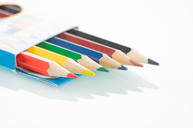 Office theme Colored pencils in an open box lie on a white mirror background