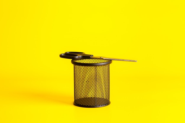 Office tool scissors in a cup on yellow