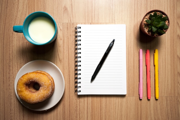 Office wood desk table with book,  supplies, donut and milk cup. Top view, Flat lay.