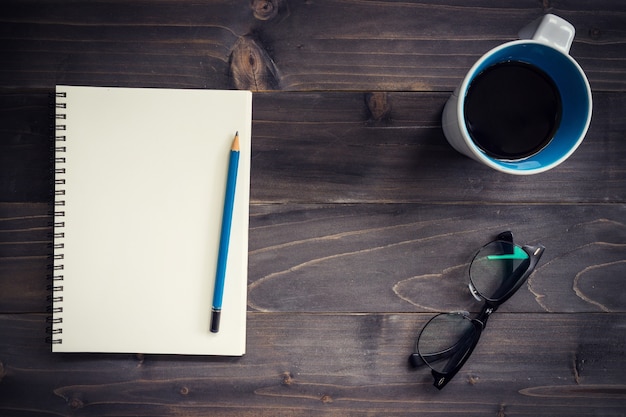 Office wood table with blank notepad, pencil, glasses and cup of coffee.