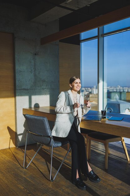 Office work attractive young female manager working in office standing in bright workspace using modern laptop computer young woman drinking delicious coffee