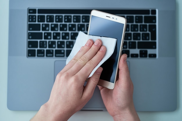 Office worker disinfects and cleans phone with antibacterial wet wipes to protect against coronavirus outbreak