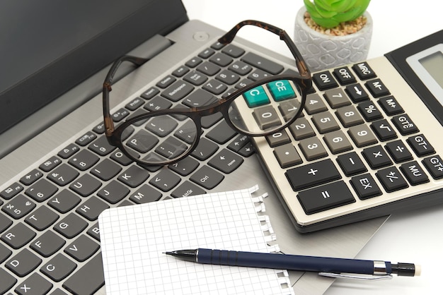 Office workstation with laptop eyeglasses notepad calculator and pen in close up high angle view