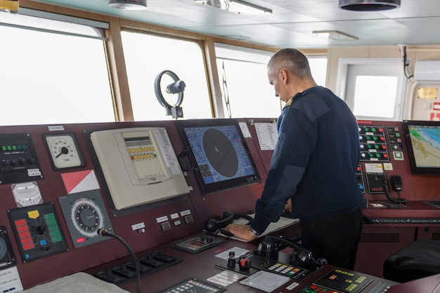 Officer on watch with radio on the navigational bridge Caucasian man in blue uniform sweater on the bridge of cargo ship