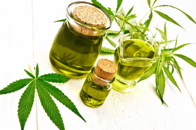 Oil hemp in gravy boat and two jars on wooden board