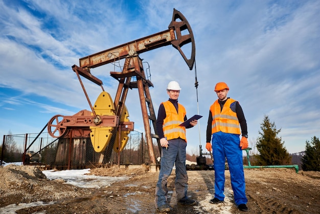 Oil rig workers standing by pump jack