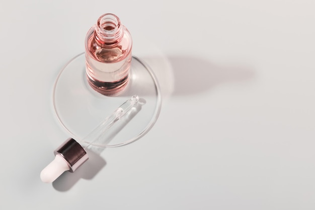 Oil or Serum bottle and pipette in petri dish on grey background Pink cosmetic product